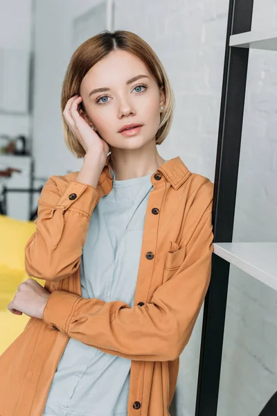 Beautiful girl standing by shelving rack and touching hair — Stock Photo