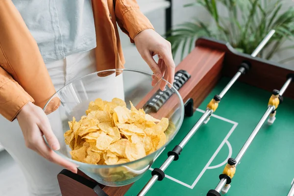 Teilansicht einer Frau, die eine Schüssel Chips hält, während sie in der Nähe eines Fußballtisches steht — Stockfoto