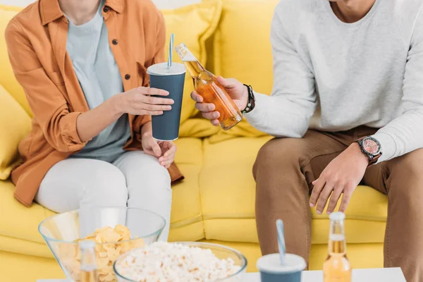 Vista parcial de la mujer con taza de papel y el hombre con botella de cerveza sentado en la mesa amarilla - foto de stock