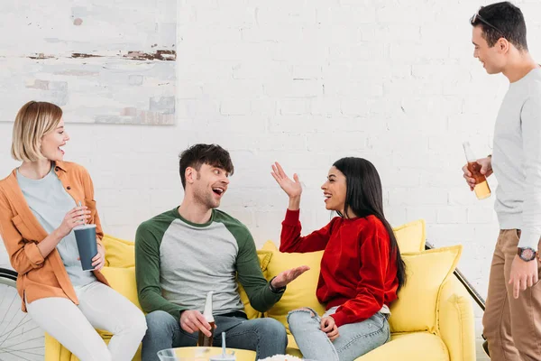 Sonrientes amigos multiculturales charlando mientras están sentados en la mesa amarilla en la sala de estar - foto de stock