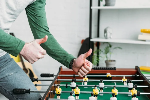 Partial view of man standing by footbal table and holding thumbs up — Stock Photo