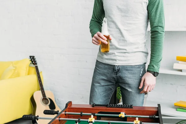 Partial view of man standing by football table and holding bottle of beer — Stock Photo