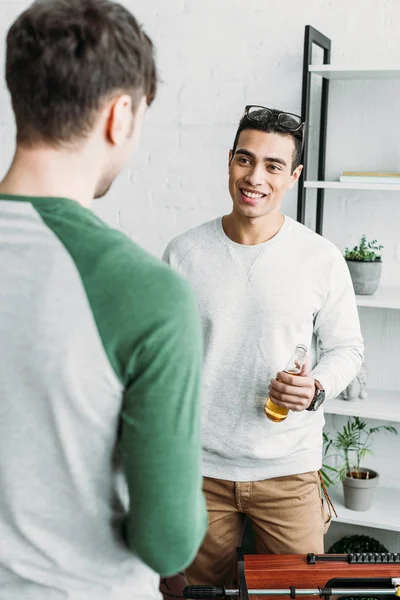 Guapo mestizo hombre de raza sosteniendo botella de cerveza y hablando con amigo - foto de stock