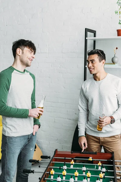 Lächelnde multikulturelle Freunde stehen am Tischkicker und halten Bierflaschen in der Hand — Stockfoto