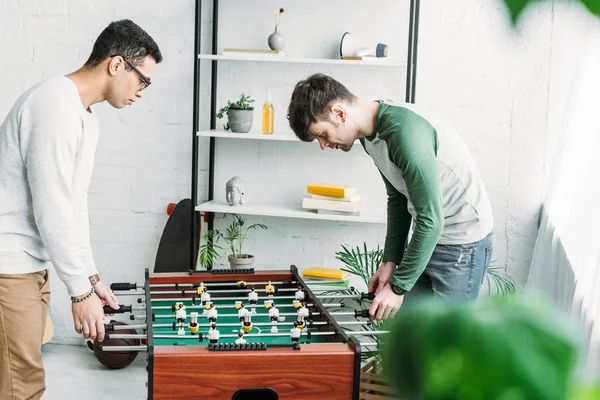 Amigos multiculturales jugando al futbolín en la amplia sala de estar - foto de stock