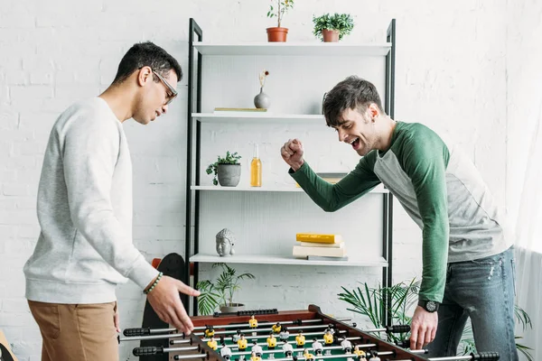 Multicultural friends playing table football in living room — Stock Photo