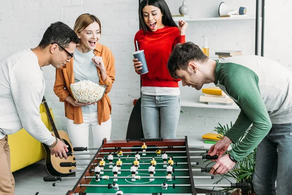 Amigos multiculturales que se divierten, los hombres jugando al futbolín mientras las niñas viendo el juego - foto de stock