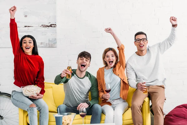 Multicultural excited friends drinking beer and wine and eating snacks at home party — Stock Photo