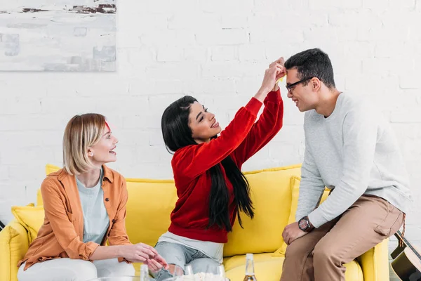 Amigos multiculturales que se divierten mientras están sentados en un sofá amarillo - foto de stock