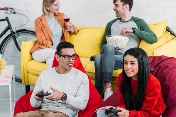 Allegri amici multiculturali giocare al videogioco e godersi bevande e spuntini — Foto stock