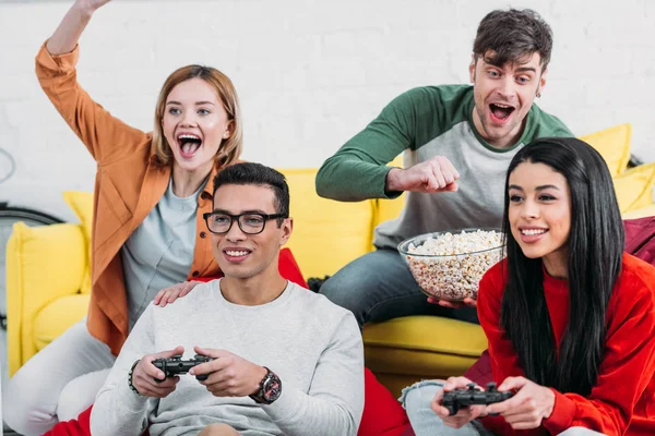 Amigos multiculturais se divertindo na festa em casa, jogando videogame e desfrutando de bebidas e lanches — Fotografia de Stock