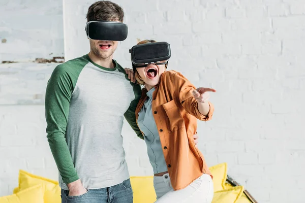 Amigos reaccionan emocionalmente mientras usan auriculares de realidad virtual en casa - foto de stock