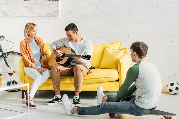 Sonriente hombre de raza mixta tocando la guitarra para amigos multiculturales en casa - foto de stock