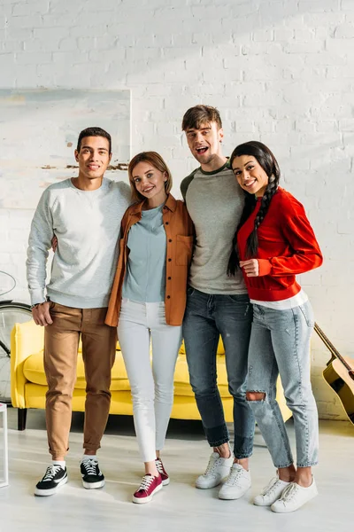 Amici multietnici sorridenti in piedi insieme in salotto e guardando la fotocamera — Foto stock