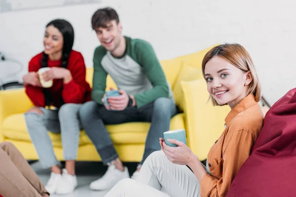 Amigos multiculturales felices tomando café mientras están sentados en la sala de estar - foto de stock