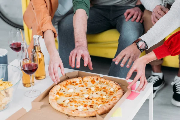 Vista recortada de hombres y mujeres estirando las manos a la pizza - foto de stock
