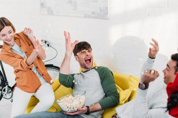 Amigos multiculturales tonteando y lanzándose palomitas de maíz - foto de stock