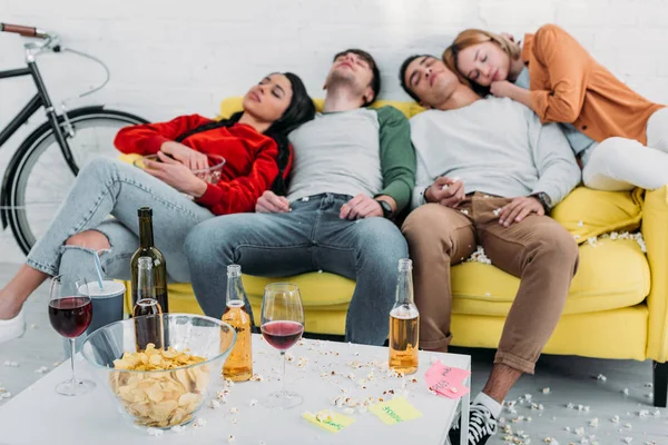 Виснажені мультикультурні друзі сплять на жовтому дивані у вітальні — стокове фото