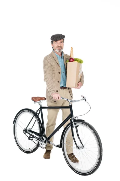 Aposentado alegre sorrindo saco de papel de capuz inteiro com mantimentos e bicicleta isolada em branco — Fotografia de Stock