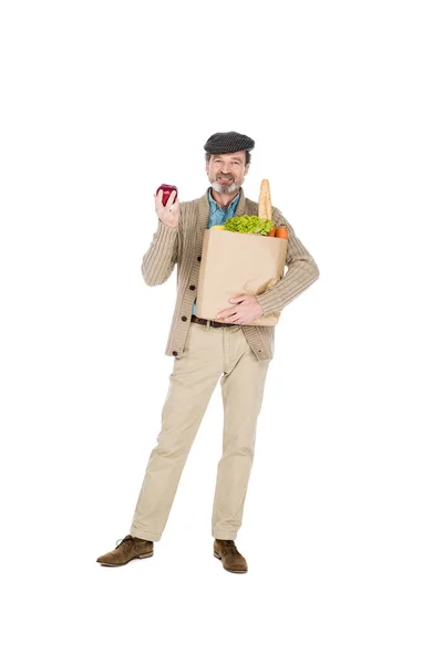 Веселий старший чоловік тримає яблуко і паперовий мішок з продуктами ізольовані на білому — стокове фото