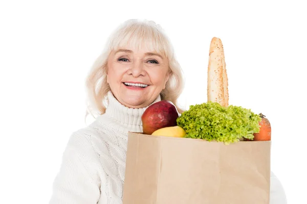 Cheerful senior woman holding paper bag with groceries isolated on white — Stock Photo