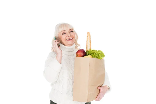 Glückliche Seniorin hält Papiertüte mit Lebensmitteln auf weißem Grund — Stockfoto