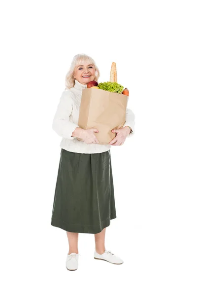 Smiling senior woman holding paper bag with groceries isolated on white — Stock Photo