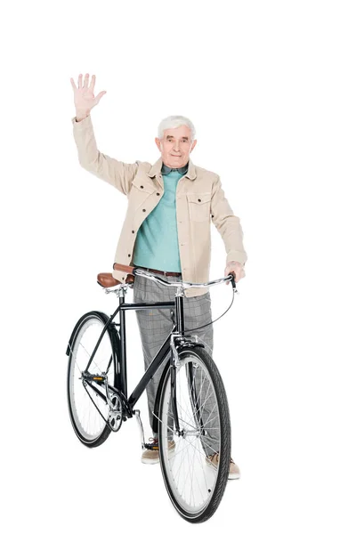 Alegre aposentado homem segurando bicicleta e mão acenando isolado no branco — Stock Photo