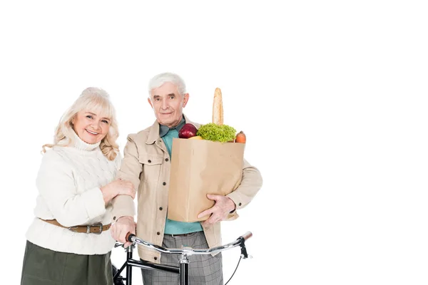 Esposa alegre de pé com o marido aposentado segurando bicicleta e saco de papel isolado no branco — Fotografia de Stock