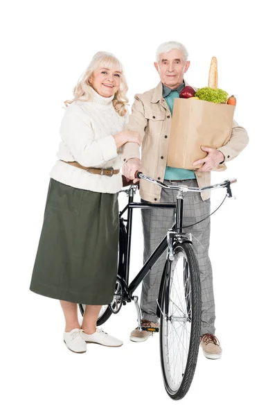 Feliz esposa de pie con el marido jubilado sosteniendo bicicleta y bolsa de papel aislado en blanco - foto de stock