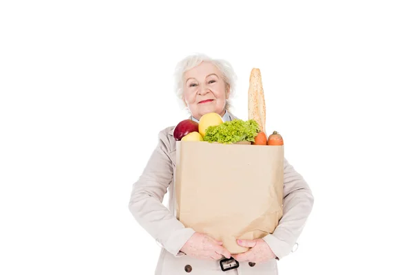 Mujer alegre con pelo gris sosteniendo bolsa de papel con comestibles aislados en blanco - foto de stock