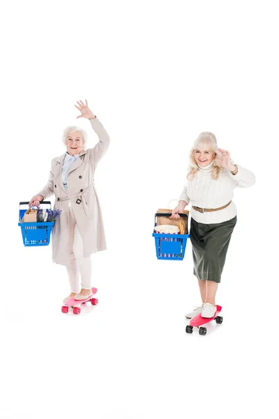 Felice donne anziane cavalcando penny board e tenendo cestini della spesa idolatrato su bianco — Foto stock
