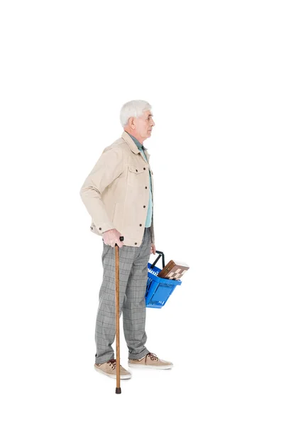 Hombre retirado sosteniendo cesta de la compra y de pie con bastón aislado en blanco - foto de stock