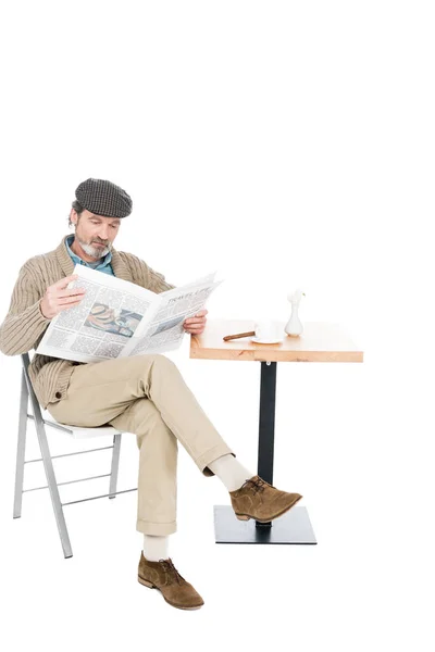 Älterer Mann liest Zeitung, während er mit überkreuzten Beinen auf weißem Stuhl sitzt — Stockfoto