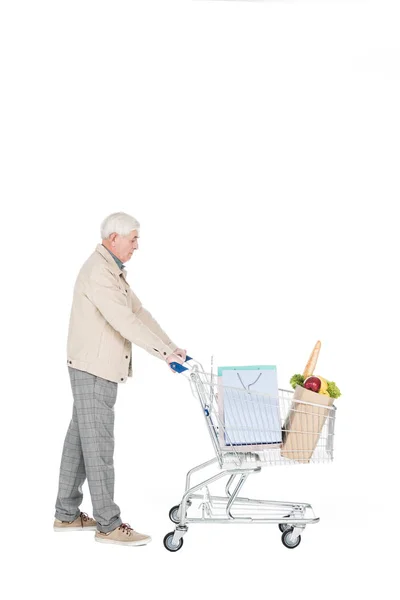 Uomo in pensione che cammina con carrello della spesa con borse della spesa e sacchetto di carta con generi alimentari isolati su bianco — Foto stock