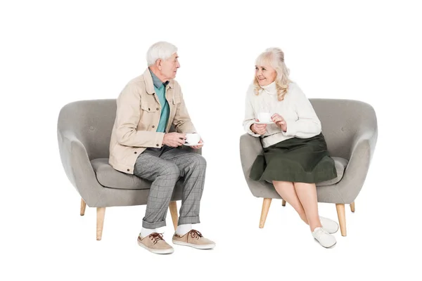 Щасливий чоловік у відставці дивиться на дружину, тримає чашку з чаєм, сидячи в кріслі ізольовано на білому — стокове фото