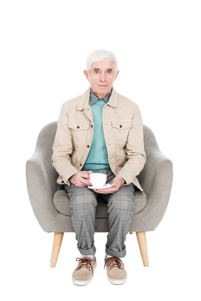 Retired man sitting in armchair with cup of tea isolated on white — Stock Photo