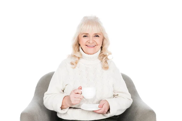 Smiling senior woman sitting in armchair with cup of tea isolated on white — Stock Photo