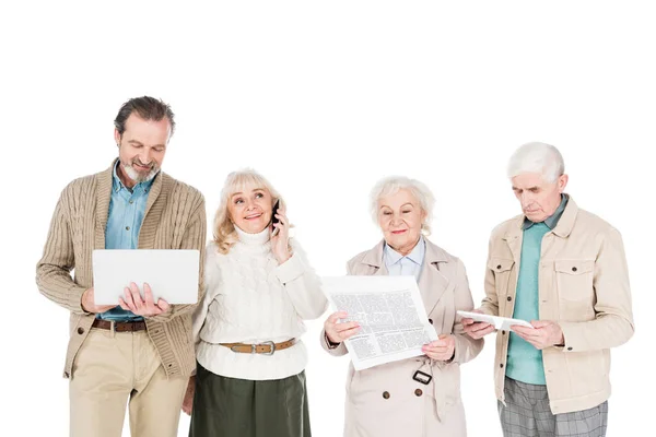 Senior people standing with gadgets near woman with newspaper isolated on white — Stock Photo