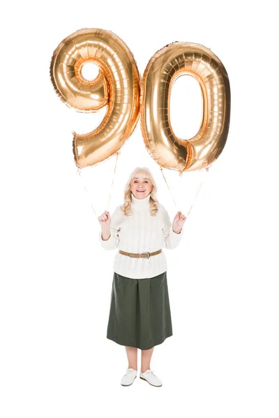 Alegre anciana sosteniendo 90 globos dorados aislados en blanco - foto de stock