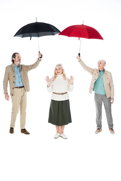 Cheerful senior woman standing under umbrellas in hands of retired men isolated on white — Stock Photo