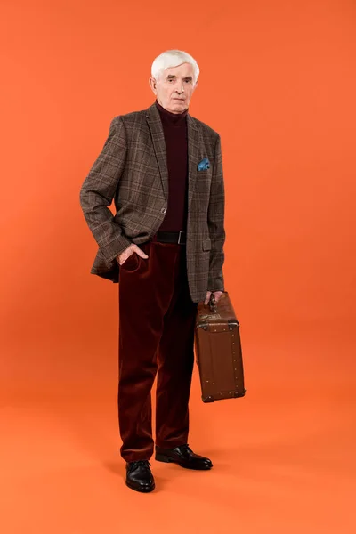 Trendy senior man holding briefcase while standing on orange background — Stock Photo