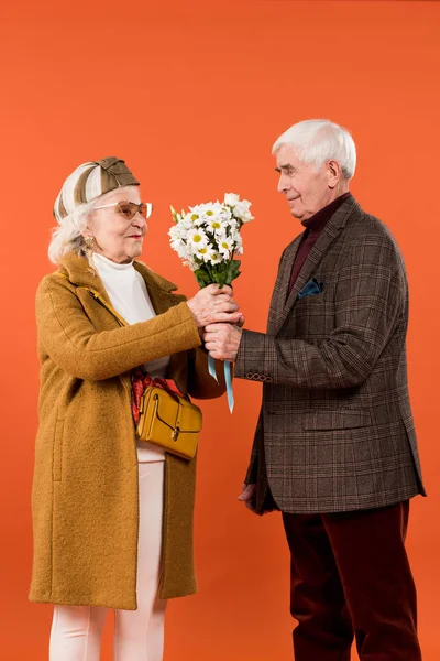 Homem sênior alegre dando flores para esposa feliz isolado em laranja — Fotografia de Stock