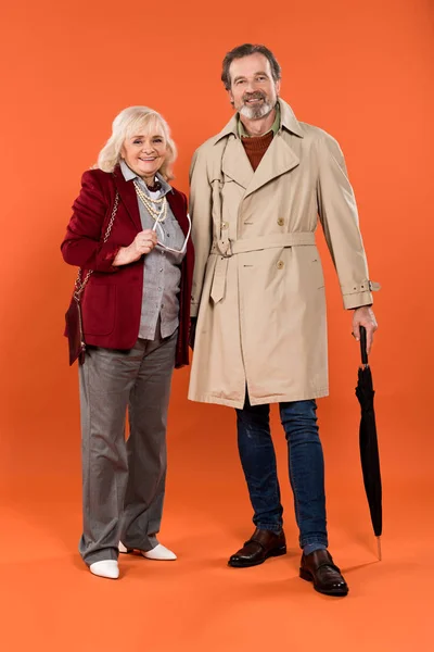 Elegante pareja de ancianos de pie y sonriendo sobre fondo naranja - foto de stock