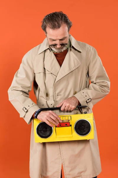 Fröhlicher Rentner drückt Taste gelbe Boombox isoliert auf orange — Stockfoto