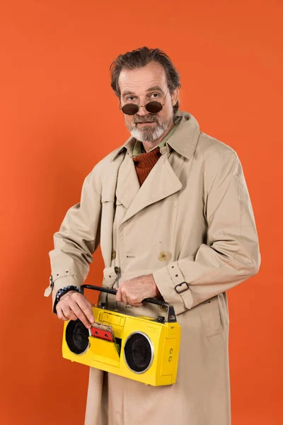 Elegante jubilado sosteniendo boombox amarillo en manos aisladas en naranja - foto de stock