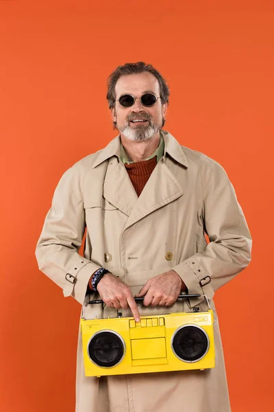 Homem aposentado alegre segurando boombox amarelo em mãos isoladas em laranja — Fotografia de Stock