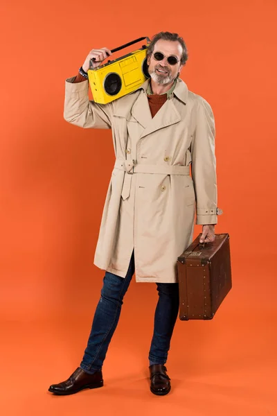 Alegre aposentado homem segurando boombox amarelo e pasta em mãos sobre fundo laranja — Fotografia de Stock