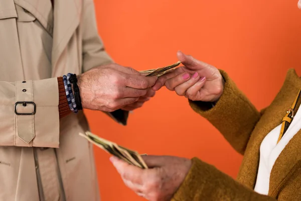Cropped view of senior couple holding dollar banknotes in hands isolated on orange — Stock Photo