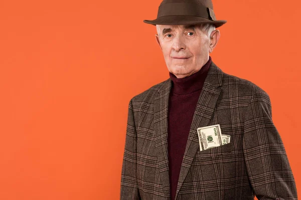 Trendiger Senior mit Hut steht mit Geld in der Tasche isoliert auf orange — Stockfoto